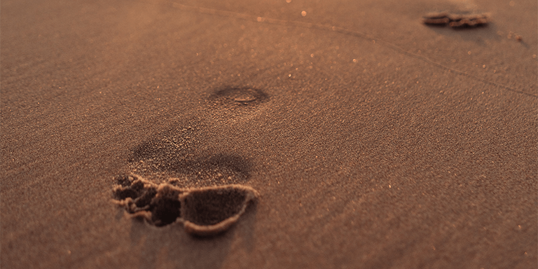 A pair of footprints in wet sand at the beach with a sunset